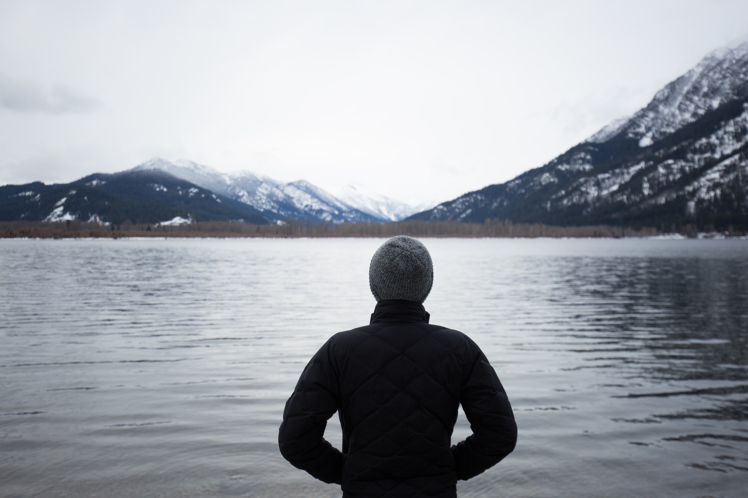 Man with back to camera looking over lake and mountains